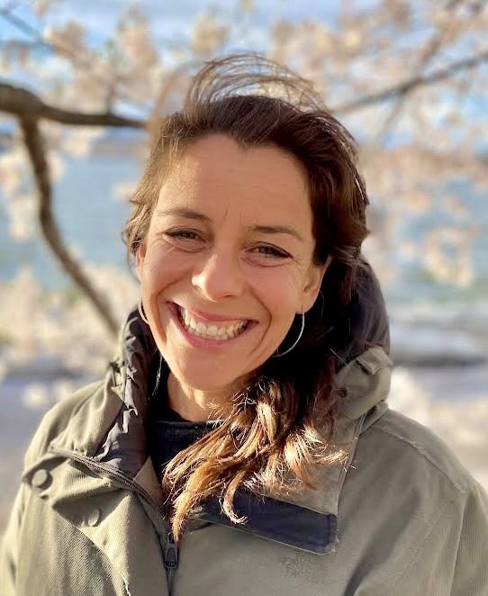 Portrait of Julia Wenegrat smiling outdoors with cherry blossoms in background.