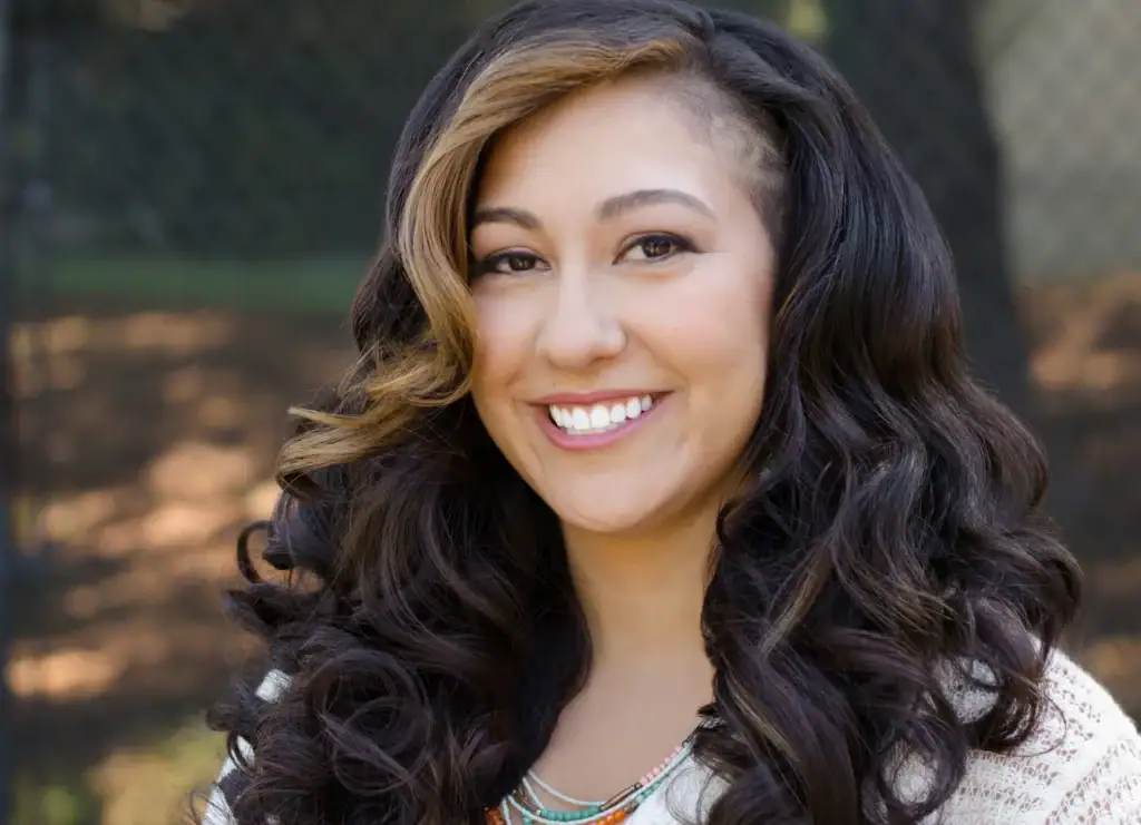 Smiling woman with dark, wavy hair outdoors for anxiety therapy.