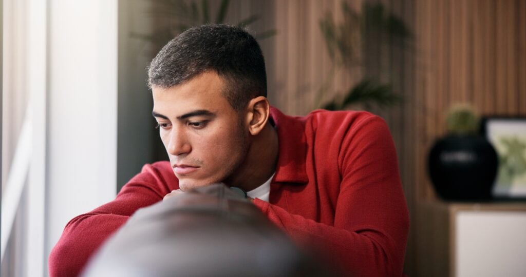Young man feeling sad and contemplative, sitting alone indoors.