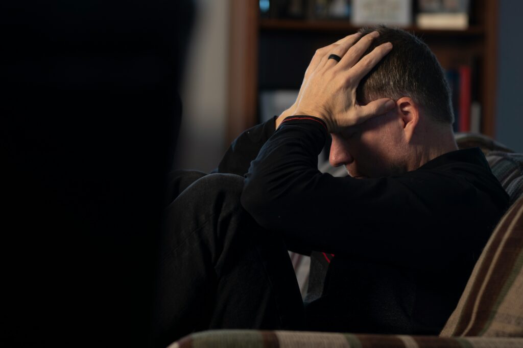 Man experiencing stress or anxiety, holding his head in a dark room.